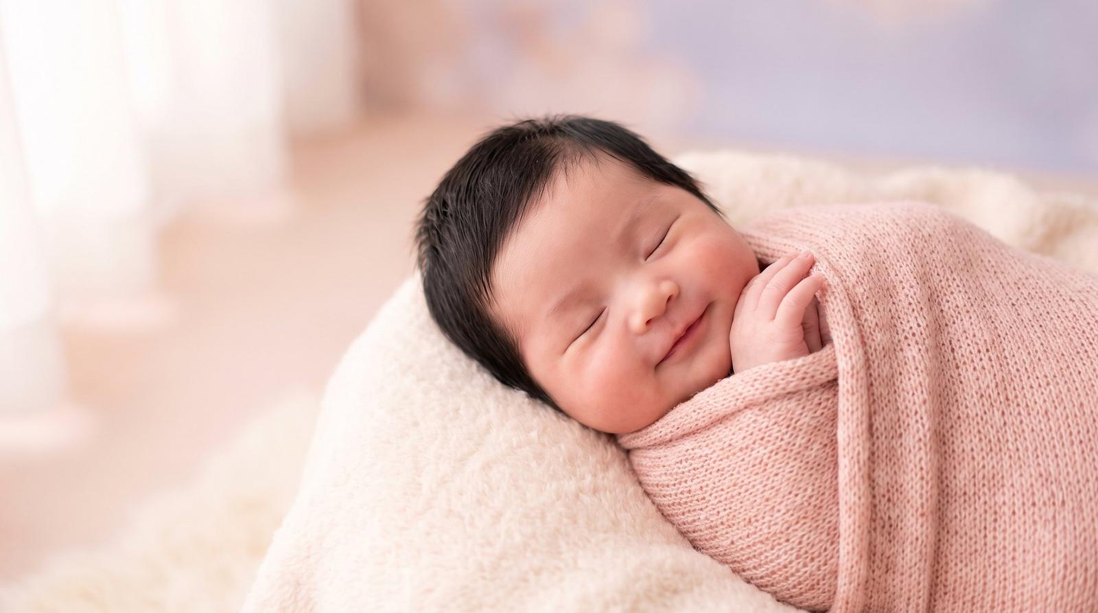 Em bé sơ sinh ngủ mỉm cười, quấn khăn len hồng